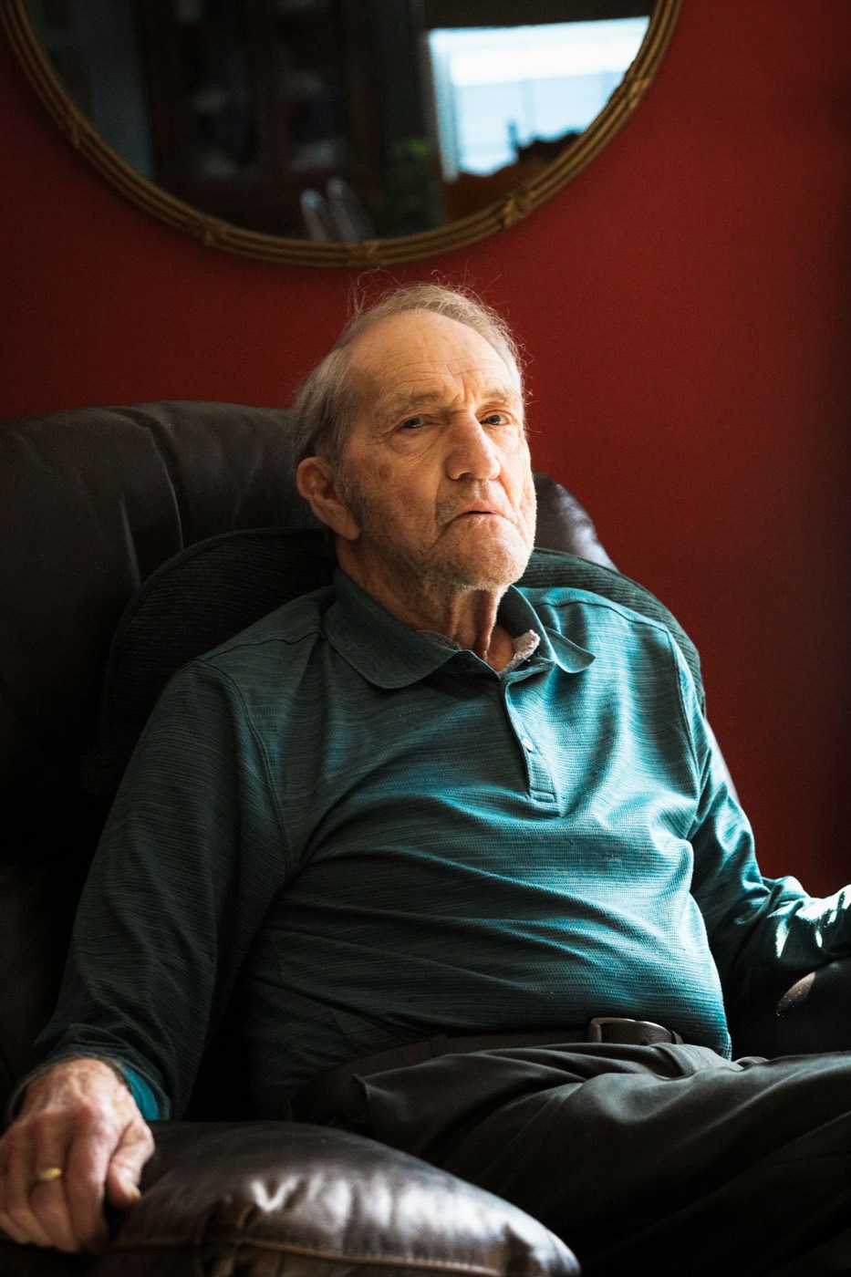 An older man in a green shirt sitting quietly in an armchair