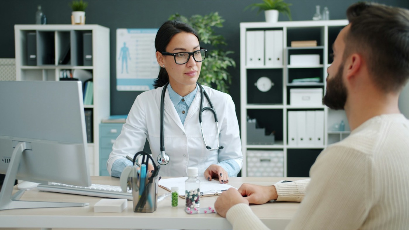 A doctor talking with a patient across a desk in a bright clinic